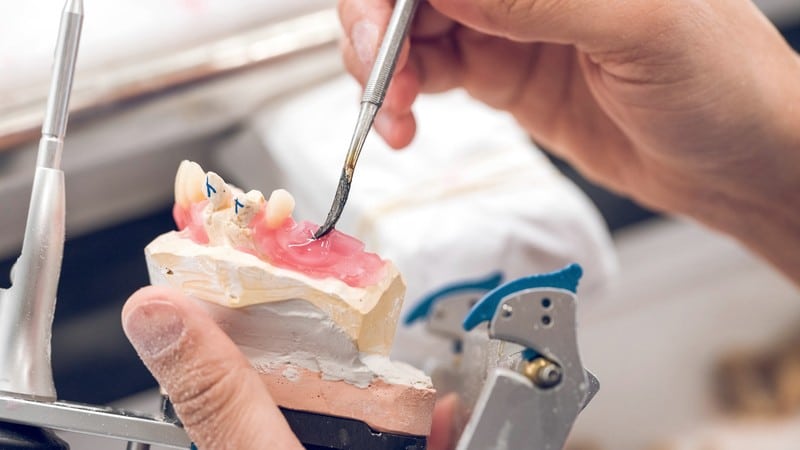 Dental technician setting a denture tooth in wax at the bench