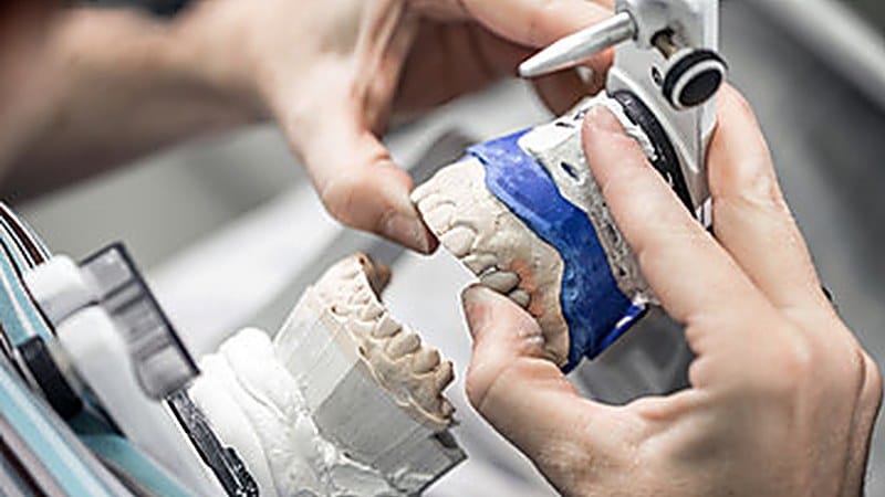 Dental lab technician finishing a denture at the bench, hands working on a model