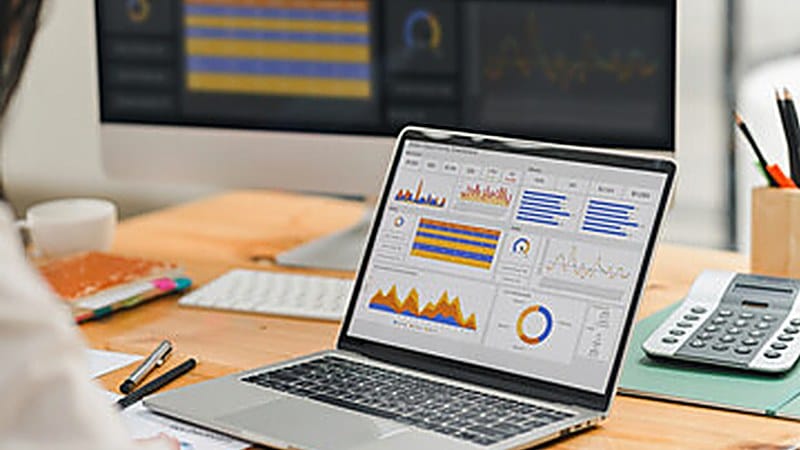 Lab manager reviewing production charts and dashboards on a laptop at a desk